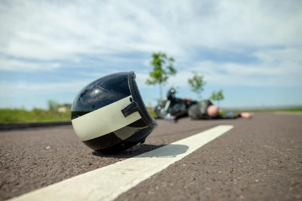 A motorcycle helmet lies on the road in front of a crashed bike and injured rider, emphasizing the need to seek medical attention before hiring a Fresno motorcycle accident lawyer.
