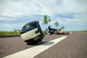 A motorcycle helmet lies on the road in front of a crashed bike and injured rider, emphasizing the need to seek medical attention before hiring a Fresno motorcycle accident lawyer.